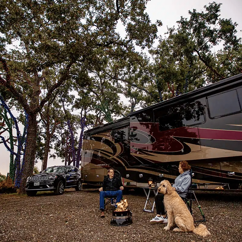 Couple sitting in front of a fire with their dog at their full hookup RV campsite at Yuletide RV Park in Madisonville, TX.